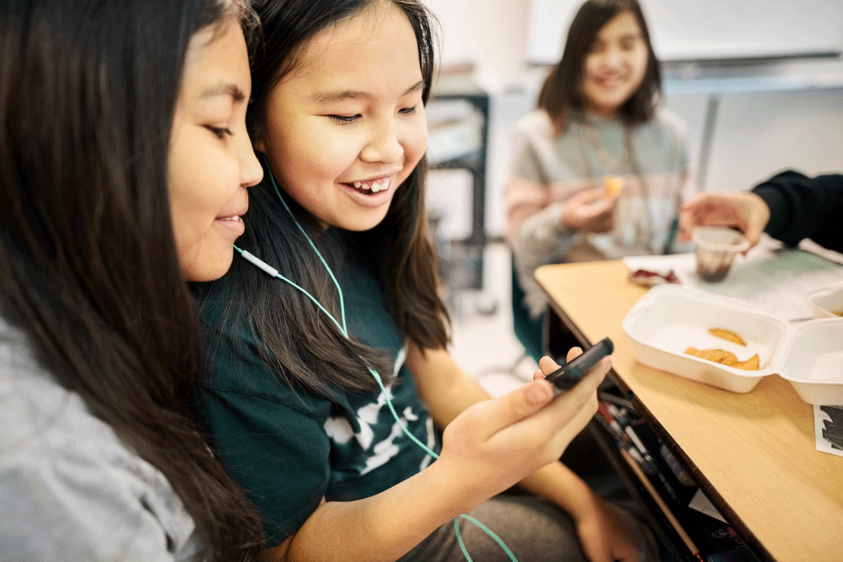 A photo of two kids looking at their mobile device.