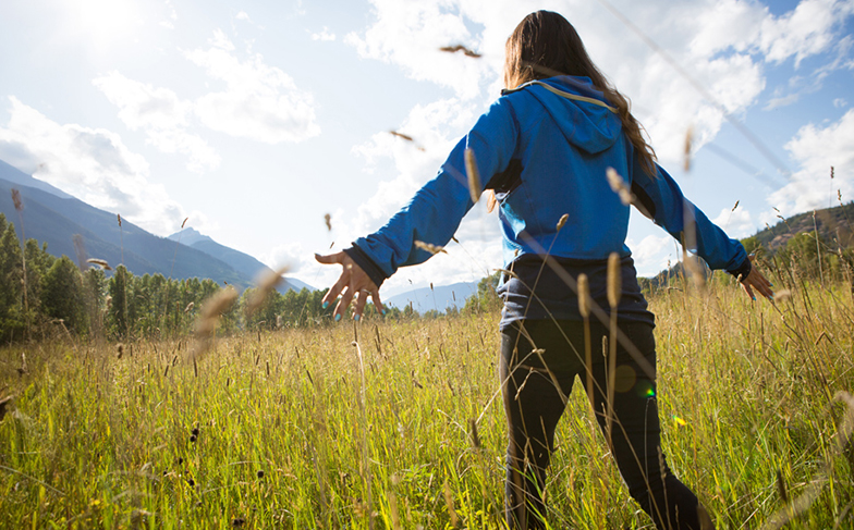 A photo of a person walking through a field of tall grasses with their arms out.
